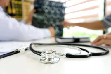 Doktor, hastanın masasındaki bilgisayarlı tedavi planıyla ilgili beyin röntgeni filmiyle birlikte belgeyi açıklıyor..