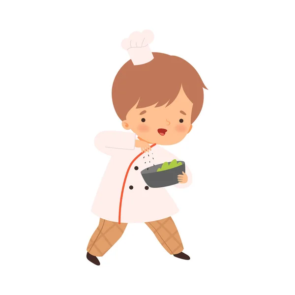 Leuke jongen met schaal, schattig klein chef-kok karakter in uniform koken in de keuken cartoon stijl vector illustratie — Stockvector