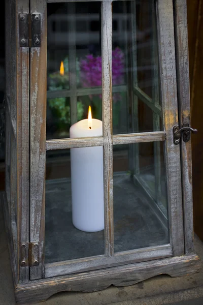 Weiße Kerze in dekorativer Laterne mit Blumen im Hintergrund — Stockfoto