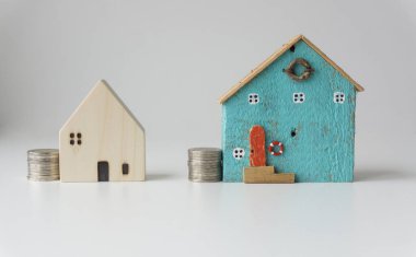 Beyaz arka planda, evin yanına para istiflenmiş iki küçük mavi ve beyaz ev gelecek için fikirler biriktiriyorlar..