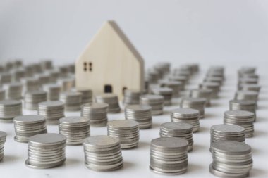 Kümelenmiş gümüş paralar ve bulanık küçük beyaz ev bozuk para sıralarının arasındadır. Ev almak için para biriktirme kavramı..