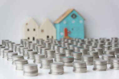 Gümüş paralar arka arkaya istiflenmiş ve üç küçük ev de arkada. Gelecekte ev almak için para biriktirme kavramı.