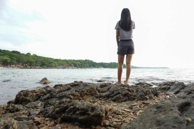 Genç bir kadın, üzgün ve üzgün bir şekilde kayaya bakıyor..