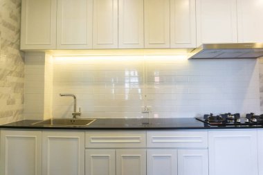 Yeni beyaz mutfak üst ve alt depo dolapları, musluk ve lavabo, güzel turuncu ışıklı kapüşonlu elektrikli hob,.