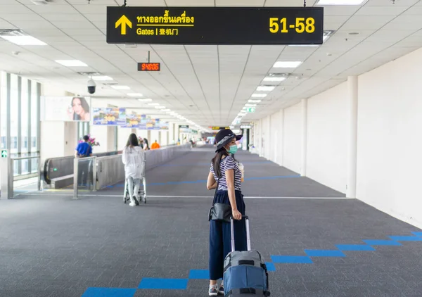 Asyalı kadın turistler mikroplardan korunmak için uluslararası havaalanlarında bavul taşıyorlar ve maske takıyorlar. Özellikle Corona virüsü ve havaalanı standartlarını takip etmek..