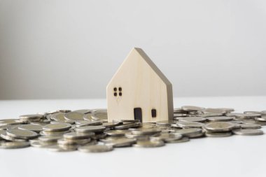 Beyaz ahşap ev yere saçılmış gümüş bir sikkeye yerleştirilmiş, beyaz arka plan, iş fikri.