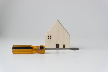 Turuncu-siyah tornavida ve küçük beyaz ahşap ev. Beyaz arka plan. Ev geliştirme fikirleri.