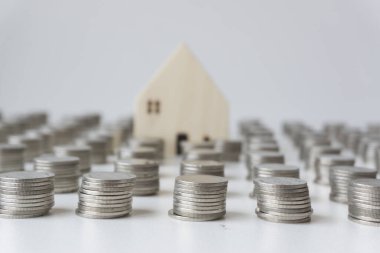 Kümelenmiş gümüş paralar ve bulanık küçük beyaz ev bozuk para sıralarının arasındadır. Ev almak için para biriktirme kavramı..