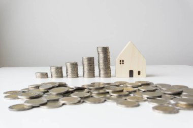 Yükseklik sırasına göre dizilmiş gümüş sikkeleri olan beyaz ahşap evler, önünde dağınık madeni paralar, beyaz arka plan, iş kavramları, iş büyümesi.