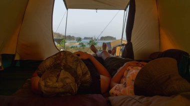 İki Asyalı turist çadırda uzanıyor, kamp tatilinde mutlular..