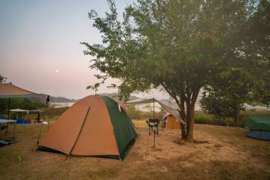 Sabahları ağaçların altında çadır ve sandalyeler. Kamp alanında ay ışığı..