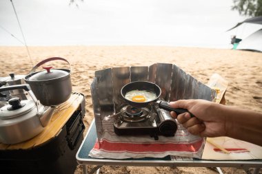 Kamp yapan turistler kızartma tavasında yumurta pişirir, kumsalda kamp yaparlar..