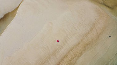 Kumsalda güneş şapkası takan ve beyaz bir kumsalda uzanan bir kadın..