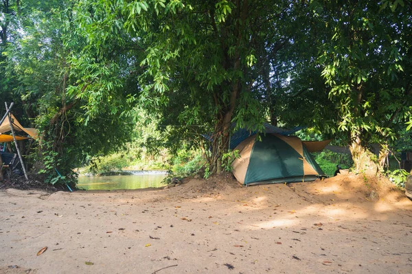 Tent under the trees, river and waterfall view, camping in the green forest.
