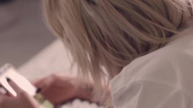 Rahat kıyafetler giymiş güzel bir Meksikalı kız cep telefonunu yavaş çekimde yatağında kontrol ediyor.