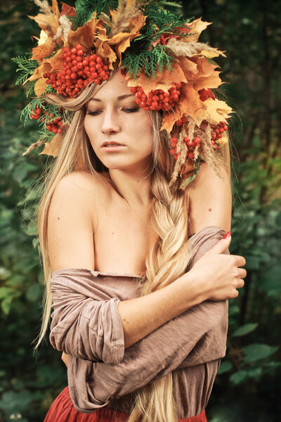 Young woman with autumn leaves in hand and fall yellow maple garden background. Woman with wreath of yellow leaves and berries on head. Autumn bright portrait sexy girl