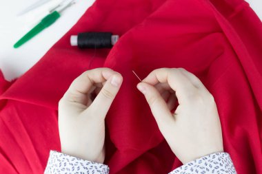 Dikiş işleminin görüntüsünü kapat. Dişi eller kırmızı kumaş diker. Bir kız elinde bir iğne tutuyor. Küçük işletme.