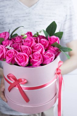 Elinde bir buket pembe gül tutan genç adam. Pembe şapka kutusunda çiçekler. Kırmızı kurdele ve yayla bağlanmış.