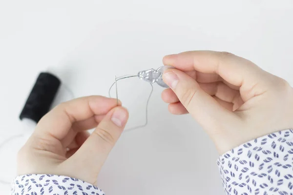 Female hands use tool to thread needles with thread. White background