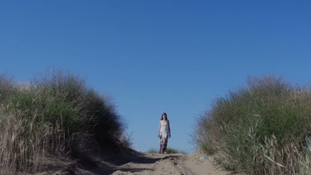 Mujer en vestido camina en un camino arenoso en verano — Vídeos de Stock