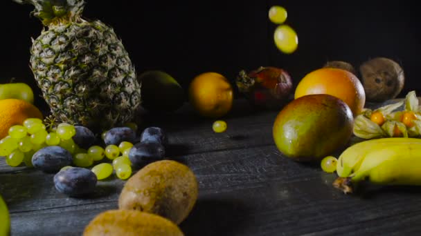 Виноград падает на деревянный стол с тропическими фруктами — стоковое видео