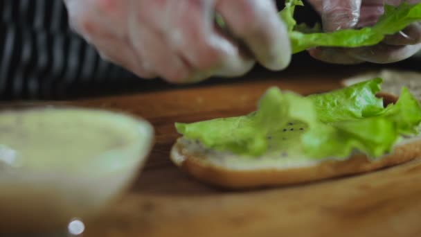 Шеф-повар кладет листья салата на бутерброд — стоковое видео