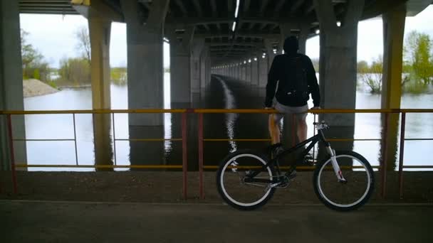 Der Typ ruht sich unter einer Brücke mit dem Fahrrad aus — Stockvideo