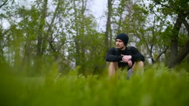 Giovane uomo seduto su erba nella foresta — Video Stock