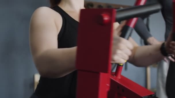 Detailní záběr na svalnaté ženy vlaky na červeném tréninkovém přístroji v tělocvičně. Školení s profesionálním trenérem — Stock video