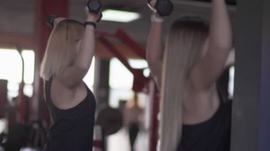 İki sarışın kadının spor salonunda dambılları kaldırışları.