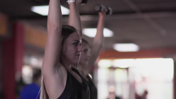 Vue latérale des femmes blondes avec ascenseur acné haltères à la salle de gym — Video