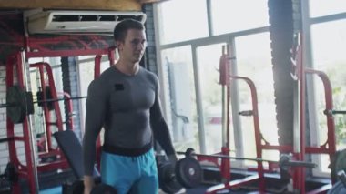 Spor salonunda halterlerle kıvrım egzersizi yapan yakışıklı bir sporcu.