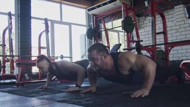 Два привлекательных атлетических культуриста мужчина и женщина делают отжимания упражнения в тренажерном зале — стоковое видео