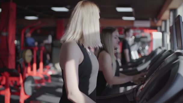 Twee fitte blonde vrouwen gebruikt loopband op te warmen voor de training — Stockvideo