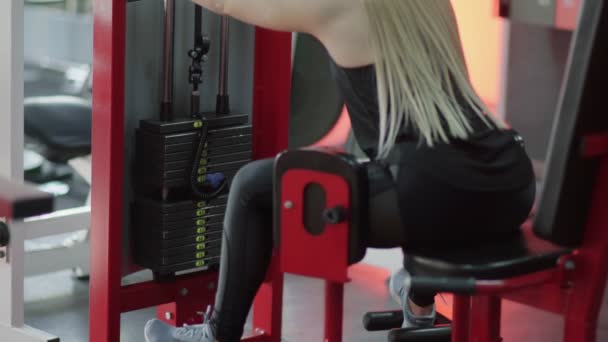 Nahaufnahme einer blonden Frau macht Beintraining auf Krafttrainer-Gerät im Fitnessstudio — Stockvideo