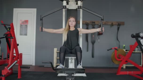 Mujer rubia entrena su pecho en simulador en el gimnasio — Vídeos de Stock