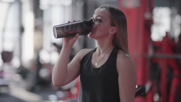 Jonge blonde vrouw drinkt water of eiwit cocktail in de sportschool — Stockvideo