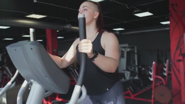 Mulher muscular aquece na máquina elíptica antes do treinamento — Vídeo de Stock