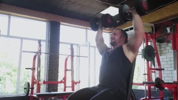 Un uomo attraente bodybuilder solleva manubri in palestra — Video Stock