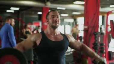 Çekici bir vücut geliştirme ustası spor salonunda halterlerle yan kaldırma egzersizi yapıyor.