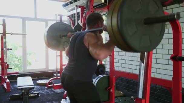 An attractive man bodybuilder does squats with barbell at gym — Stock Video