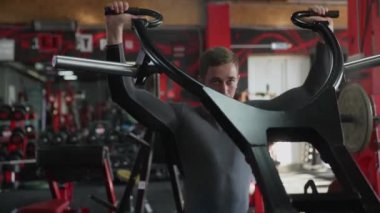 Yakışıklı sporcu spor salonundaki Güçlü Antrenör makinesine baskı yapıyor.