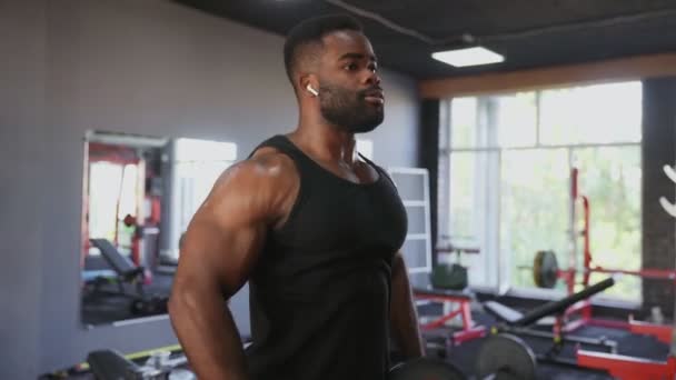 Uomo afroamericano bodybuilder con cuffie wireless esecuzione Side raise esercizio con manubri in palestra — Video Stock