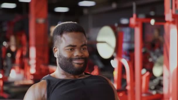 Close up de homem americano africano fisiculturista com fones de ouvido sem fio exercitando-se na máquina sentada de baixa fileira no ginásio — Vídeo de Stock