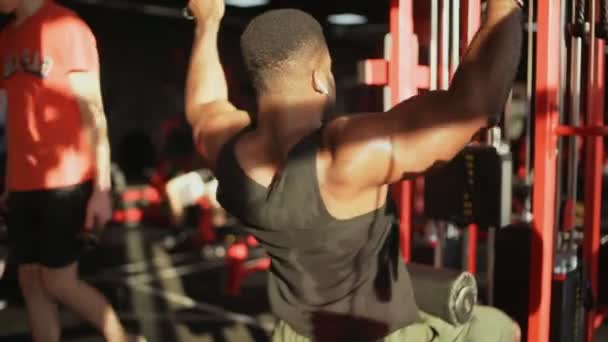 Vista posteriore dell'uomo africano americano bodybuilder con cuffie wireless che eseguono il pulldown Lat in palestra — Video Stock