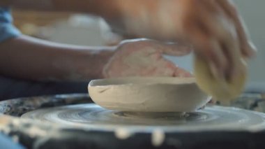 Kadın çömlekçinin yan görünüşü, bükülmüş çömlek çarkında seramik kap yapmak için sünger kullanır..
