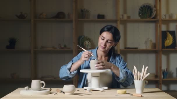 Mujer alfarero utilizando herramientas para hacer taza de arcilla de cerámica en el estudio de alfarero — Vídeos de Stock