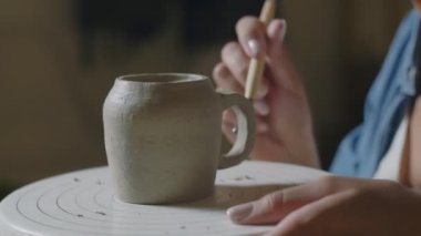 Çömlekçi kadın çömlekçiyi çömlekçi stüdyosunda seramik kilden bardak kulpu yapmak için aletler kullanarak kapatın.