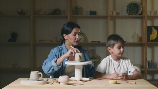 Молодая женщина учитель учит маленького мальчика, как сделать керамическую чашку — стоковое видео