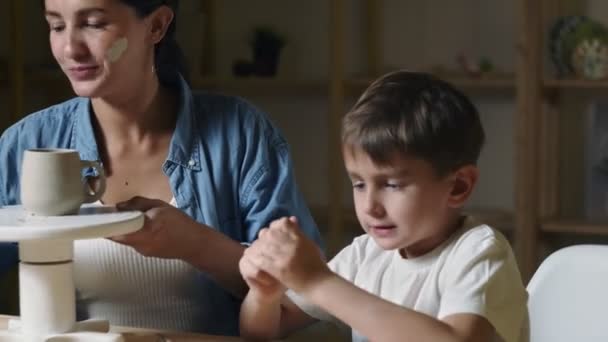 Gros plan de la jeune enseignante enseigne à un petit garçon comment faire une tasse en céramique — Video
